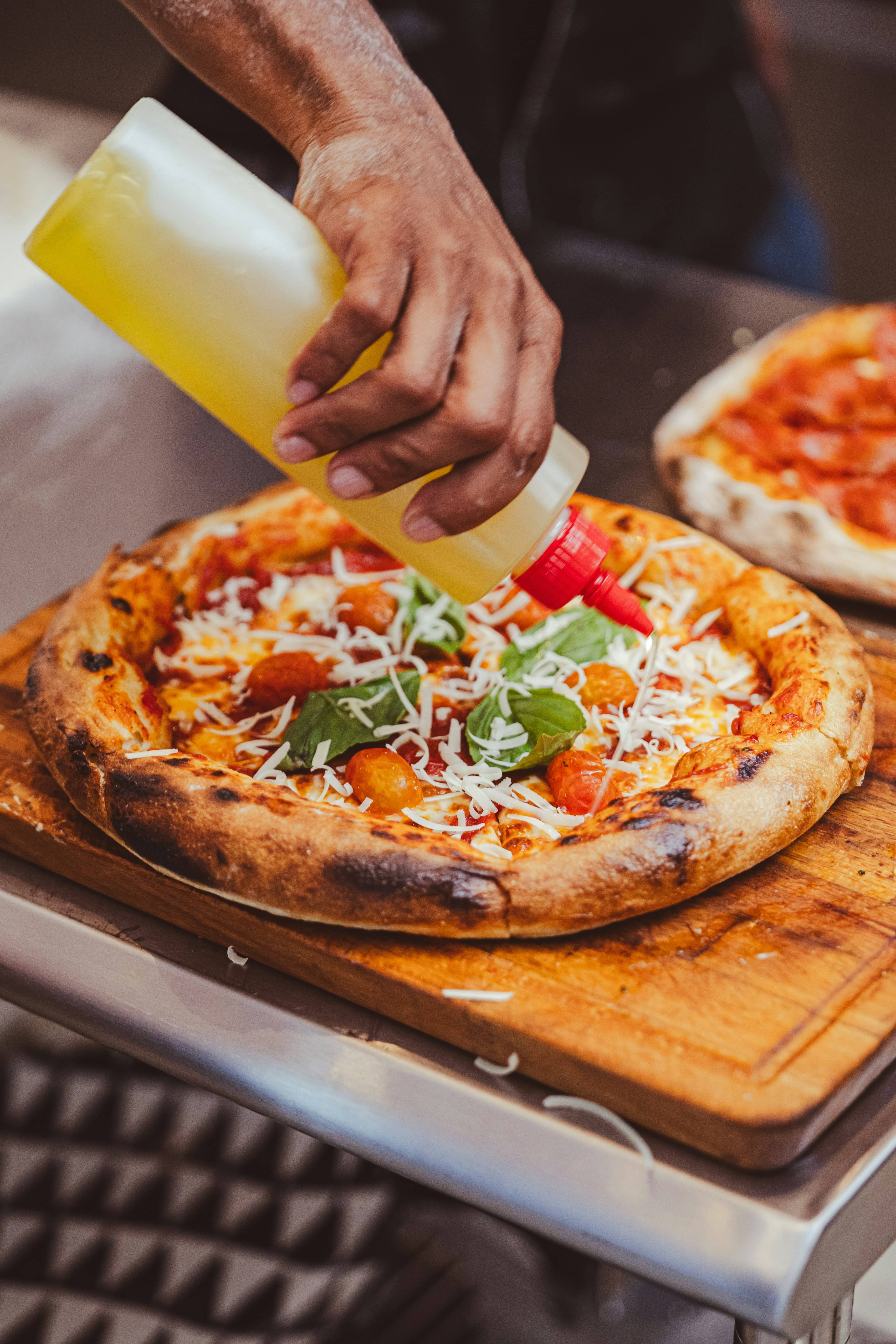 Mano che completa una pizza al banco con un filo d'olio