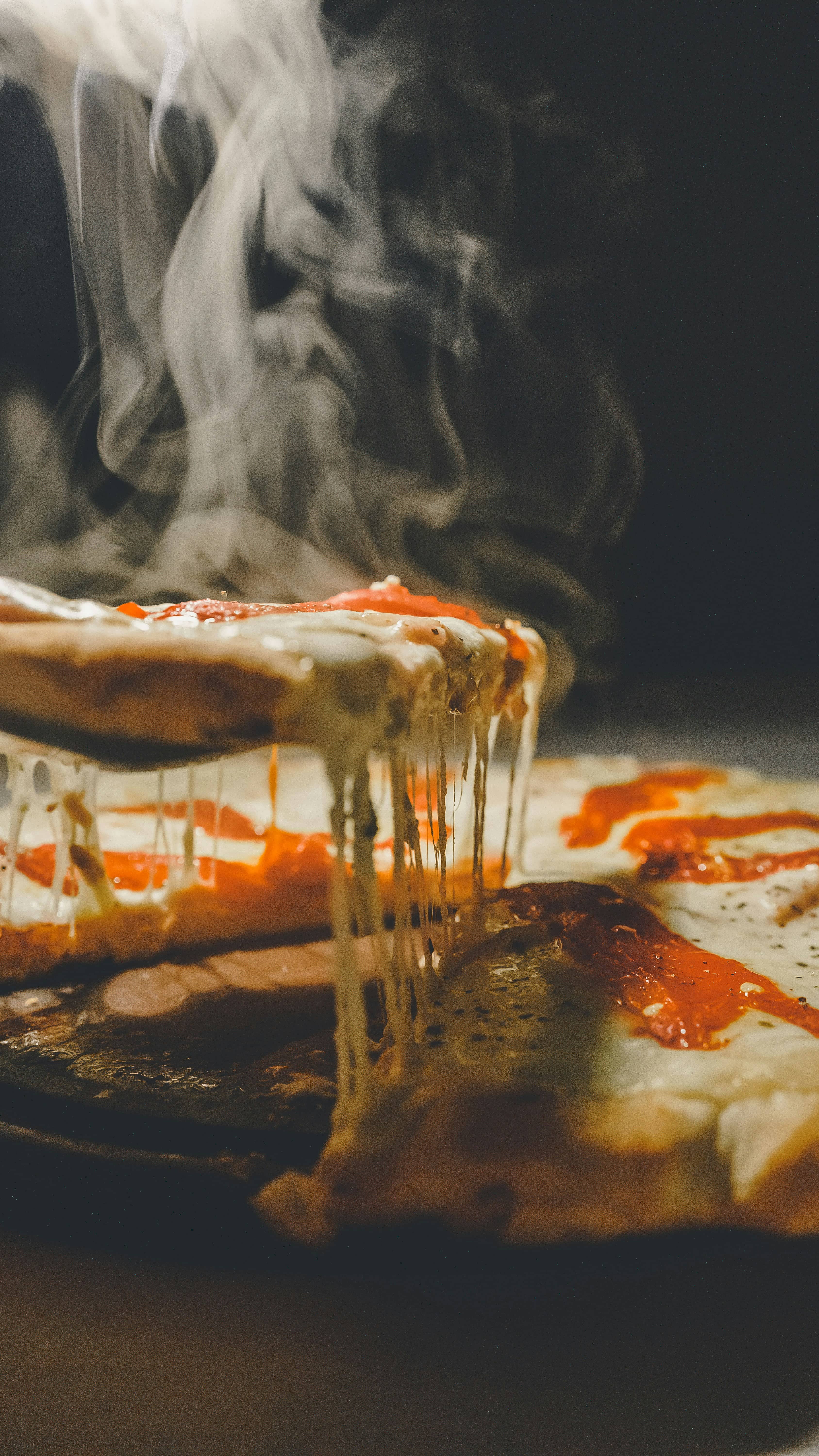 Trancio sollevato con la mozzarella filante e il vapore che sale nel buio