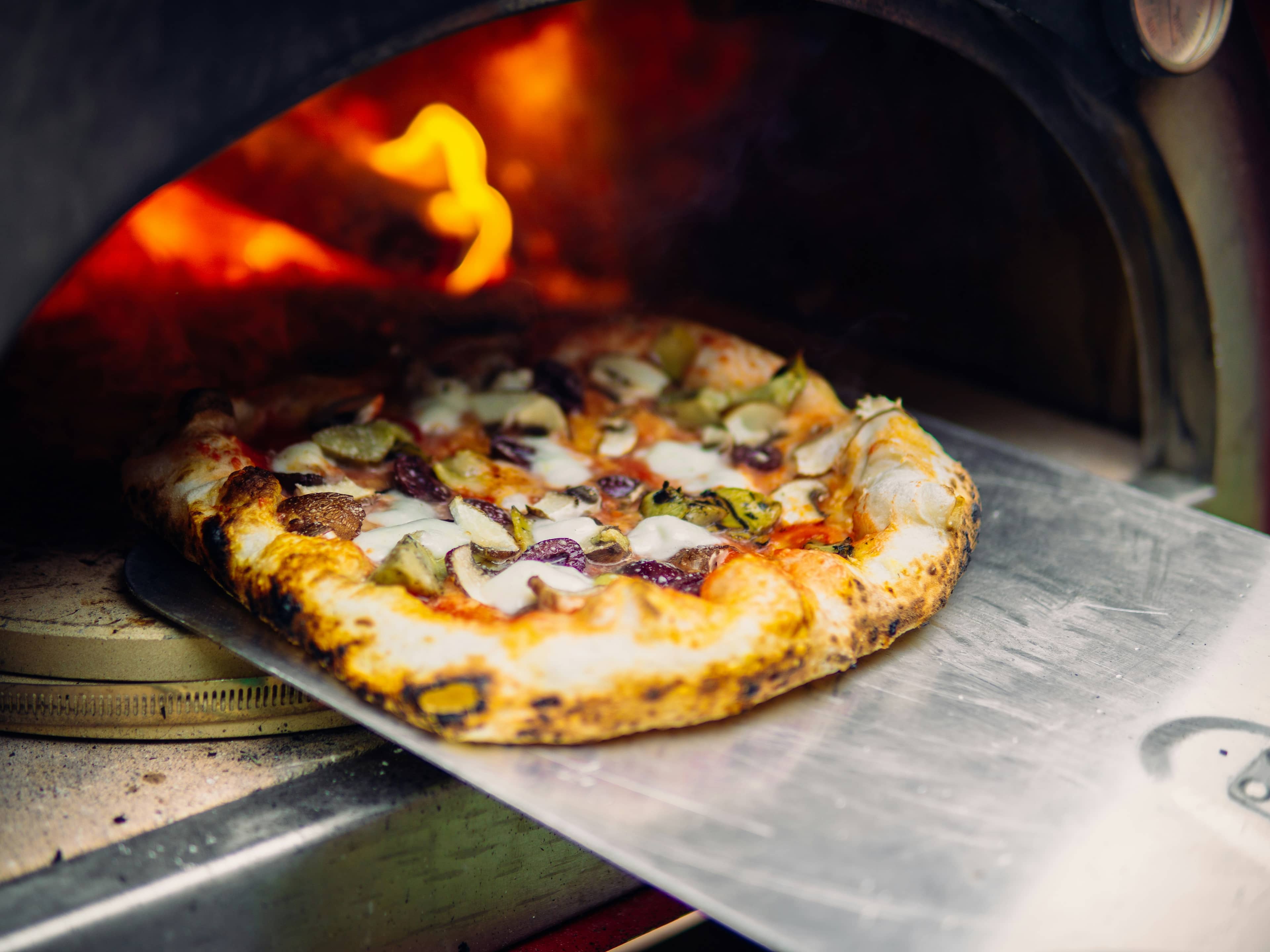 Pizza con verdure alla brace, funghi e olive sulla pala davanti alla fiamma