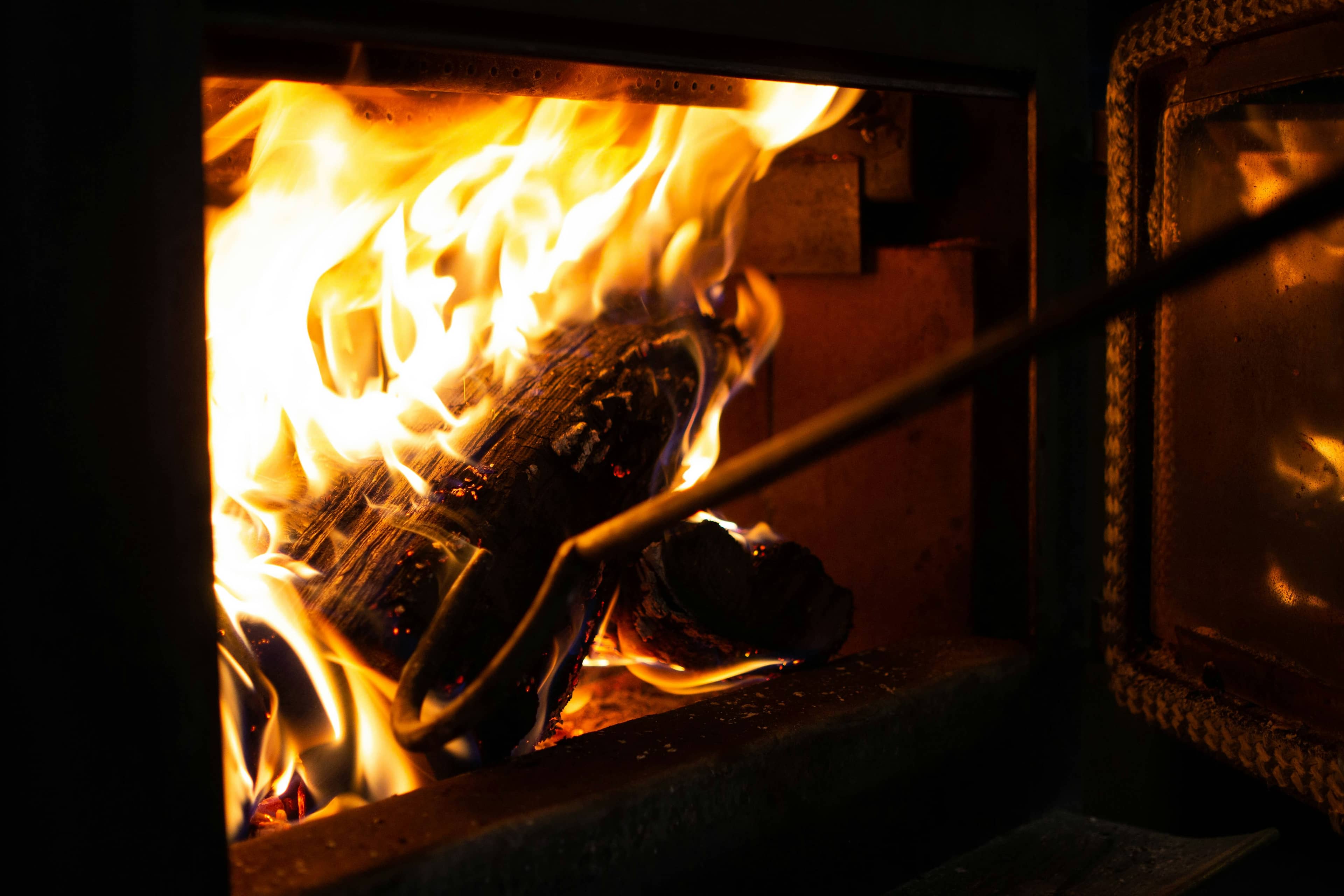Legna che brucia nel primo forno, con lo sportello aperto e l'attizzatoio
