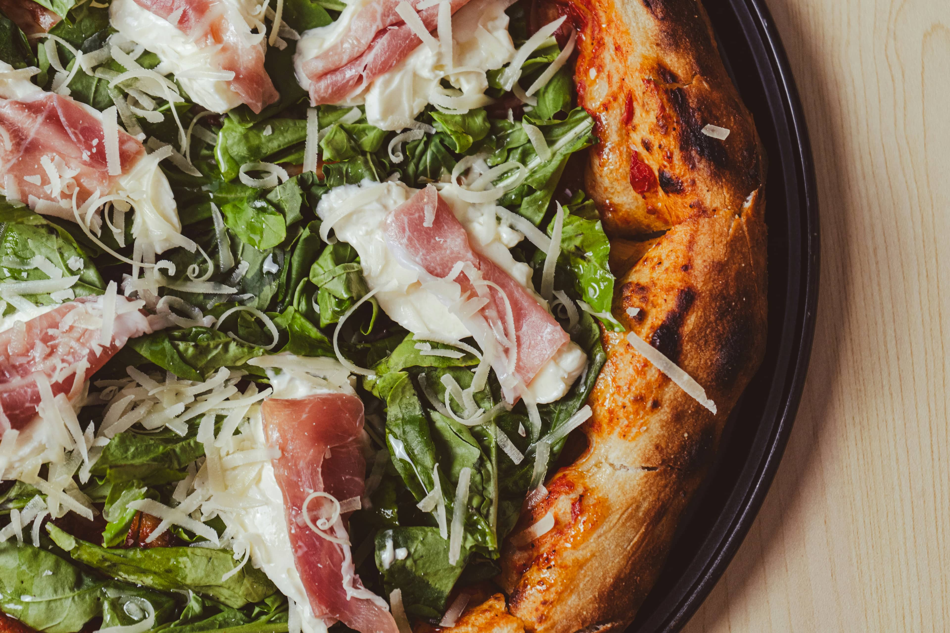 Dettaglio di pizza con rucola, crudo e scaglie di formaggio