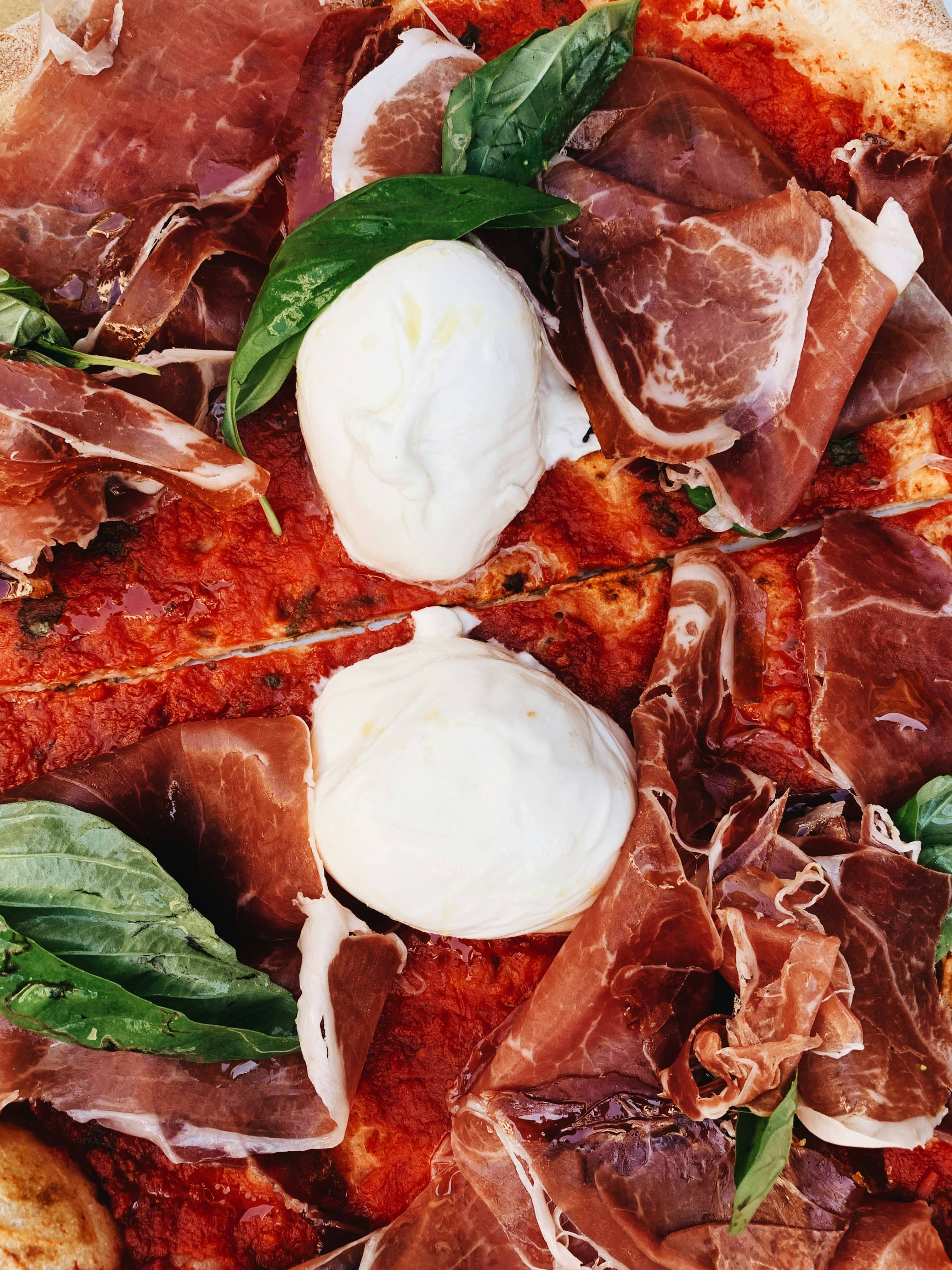 Pizza rossa con crudo e burrata vista dall'alto, tagliata a metà